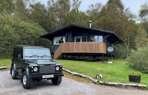 A black Land Rover parked in front of a wooden deck house with a satellite dish.