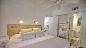 A bedroom with a wooden headboard, a large bed with white bedding, two wall-mounted lights, and a ceiling fan. - Pool view.  Upstairs unit & workspace (St Pete Beach)