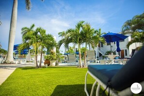 A poolside area with palm trees, lounge chairs, and a blue umbrella. - GulfSide Resort #6.  Studio on ground floor with pool views (St Pete Beach)