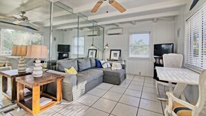 Ein Wohnzimmer mit grauem Ecksofa, einem Holztisch, einem weißen Esstisch und einem Deckenventilator.