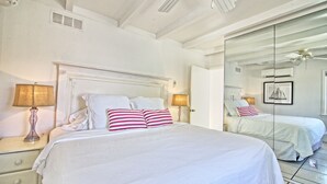Ein Hotelzimmer mit einem großen Bett, zwei Nachttischen mit Lampen, einem Deckenventilator und einem großen Spiegel, der das Zimmer reflektiert.