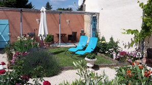 A garden with a blue chair, a white umbrella, and a table with chairs.