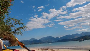 A beach with a clear sky, mountains in the background, and a boat on the water. - Planeta Banana B&B (Paraty)