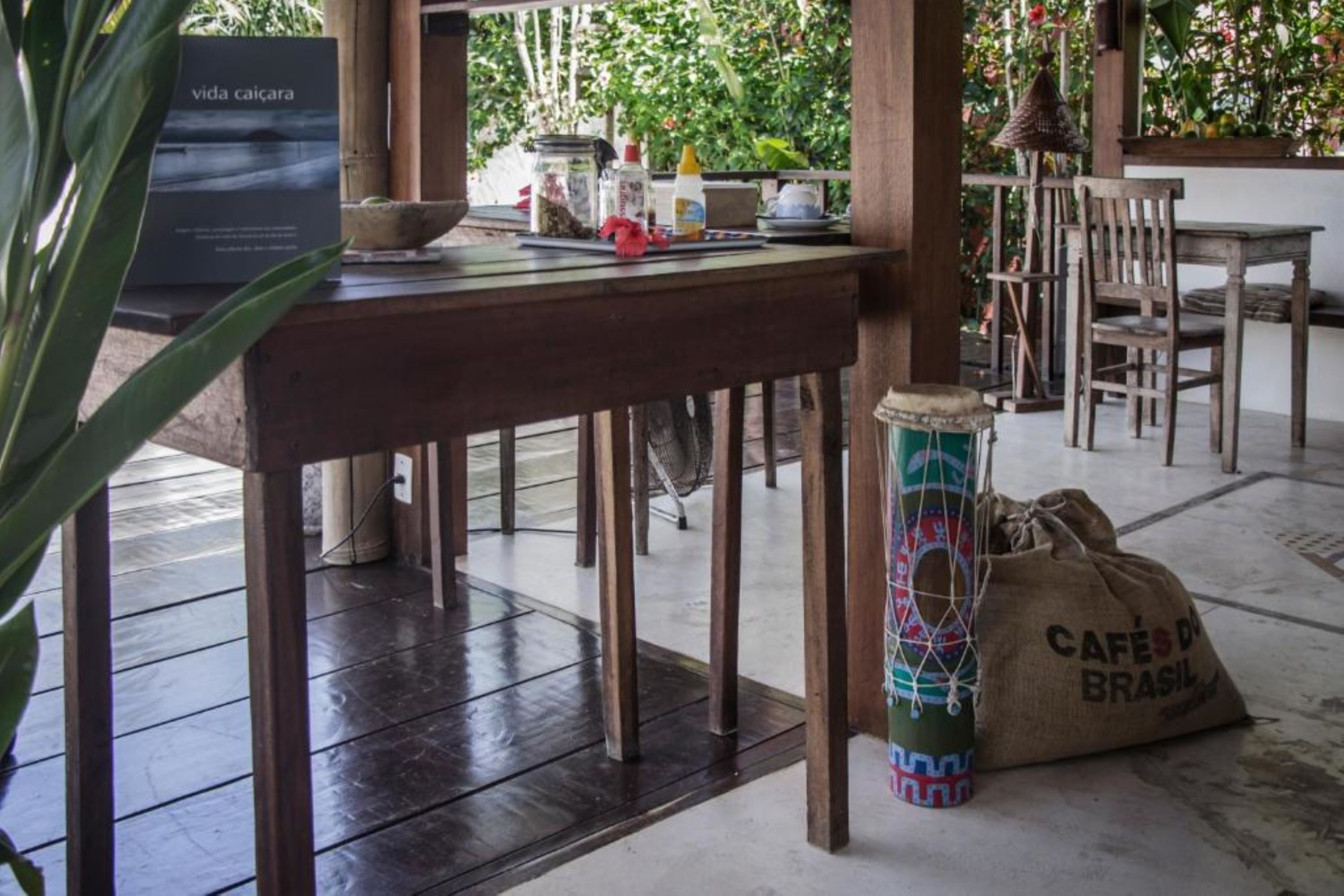Une table en bois sur laquelle est posée une pancarte indiquant « vida caicara », et un sac étiqueté « CAFÉ BRASIL » est placé sur le sol.