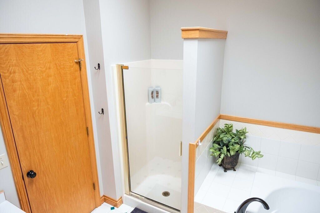Een badkamer met een houten deur, een glazen douchecabine, een wit bad en een potplant.