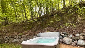 Un jacuzzi en una terraza de madera rodeado por un muro de piedra, en un entorno boscoso.