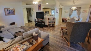 A living room with a sofa, armchair, coffee table, television, bookshelf, and a dining area with a table and chairs. - Beth`s Chalet in Pinetop (Pinetop)