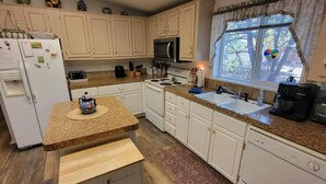 A kitchen with white cabinets, a granite countertop, a refrigerator, a microwave, a stove, a sink, and a window with a view of trees. - Beth`s Chalet in Pinetop (Pinetop)