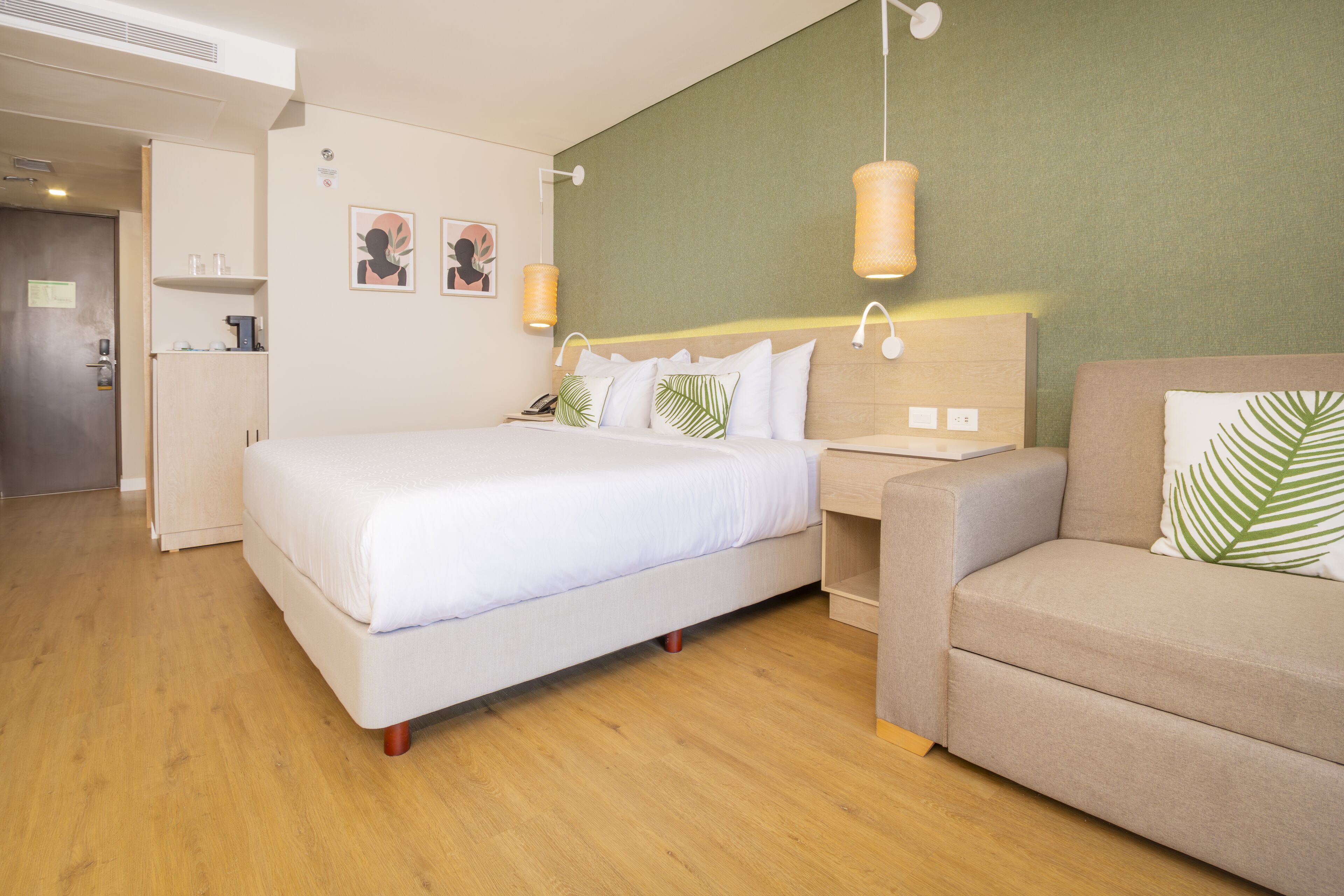 A hotel room with a bed, a sofa, a small table, and a wall-mounted lamp.