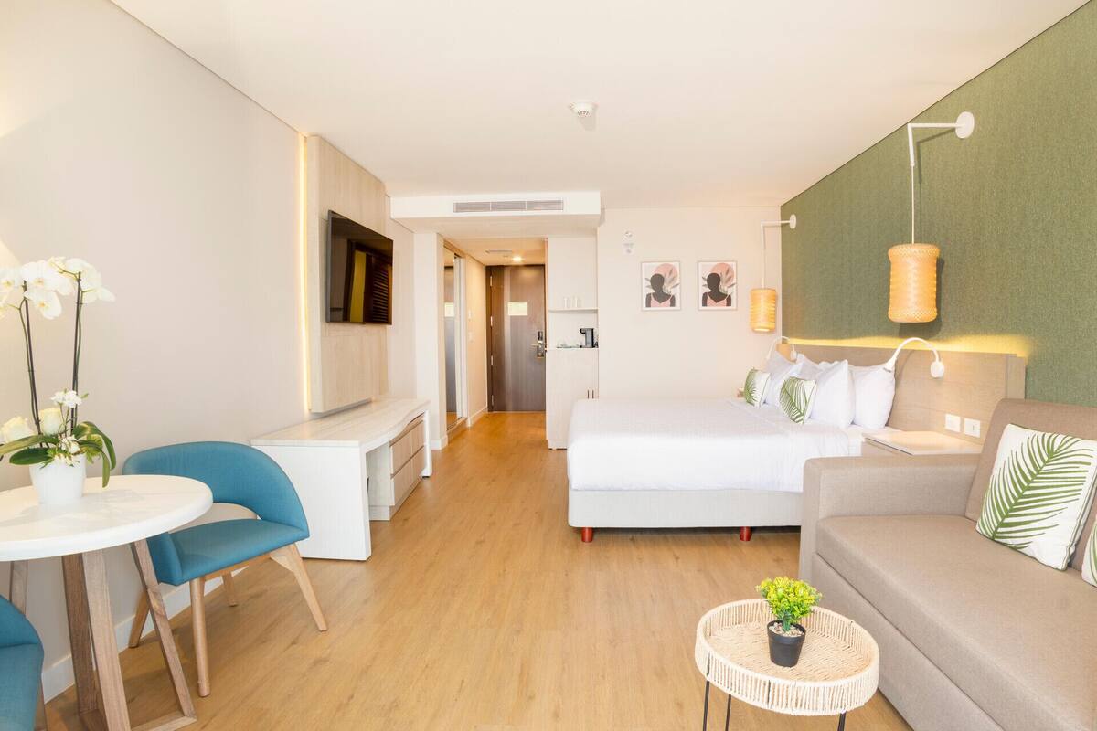 Une chambre d’hôtel comprenant un lit, un canapé, un bureau, une chaise et une petite table ronde agrémentée d’une plante.