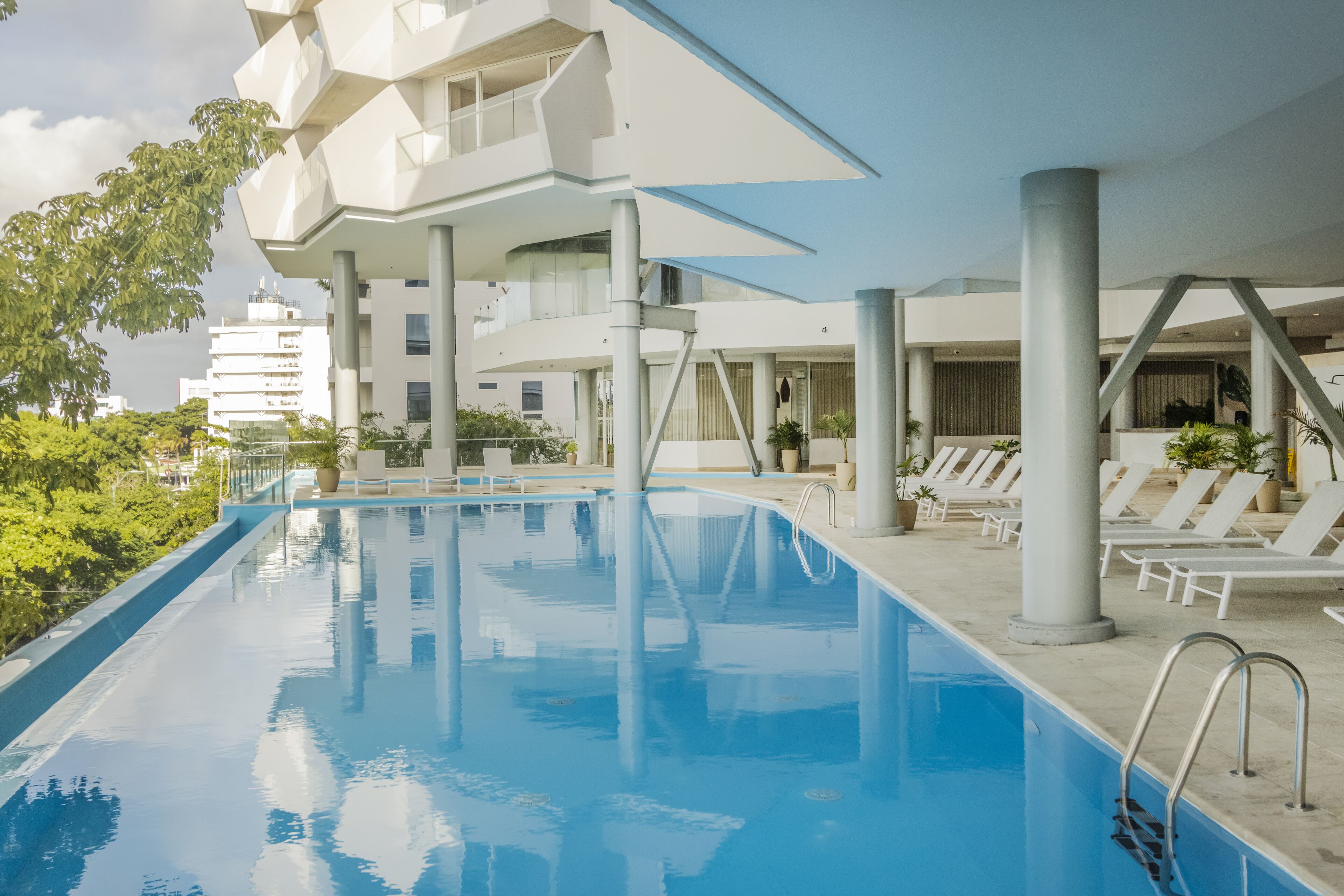 Un área de piscina moderna con arquitectura geométrica, sillones de descanso y vistas despejadas de los edificios circundantes.