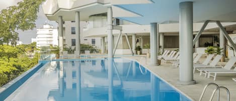 Un área de piscina moderna con arquitectura geométrica, sillones de descanso y vistas despejadas de los edificios circundantes.