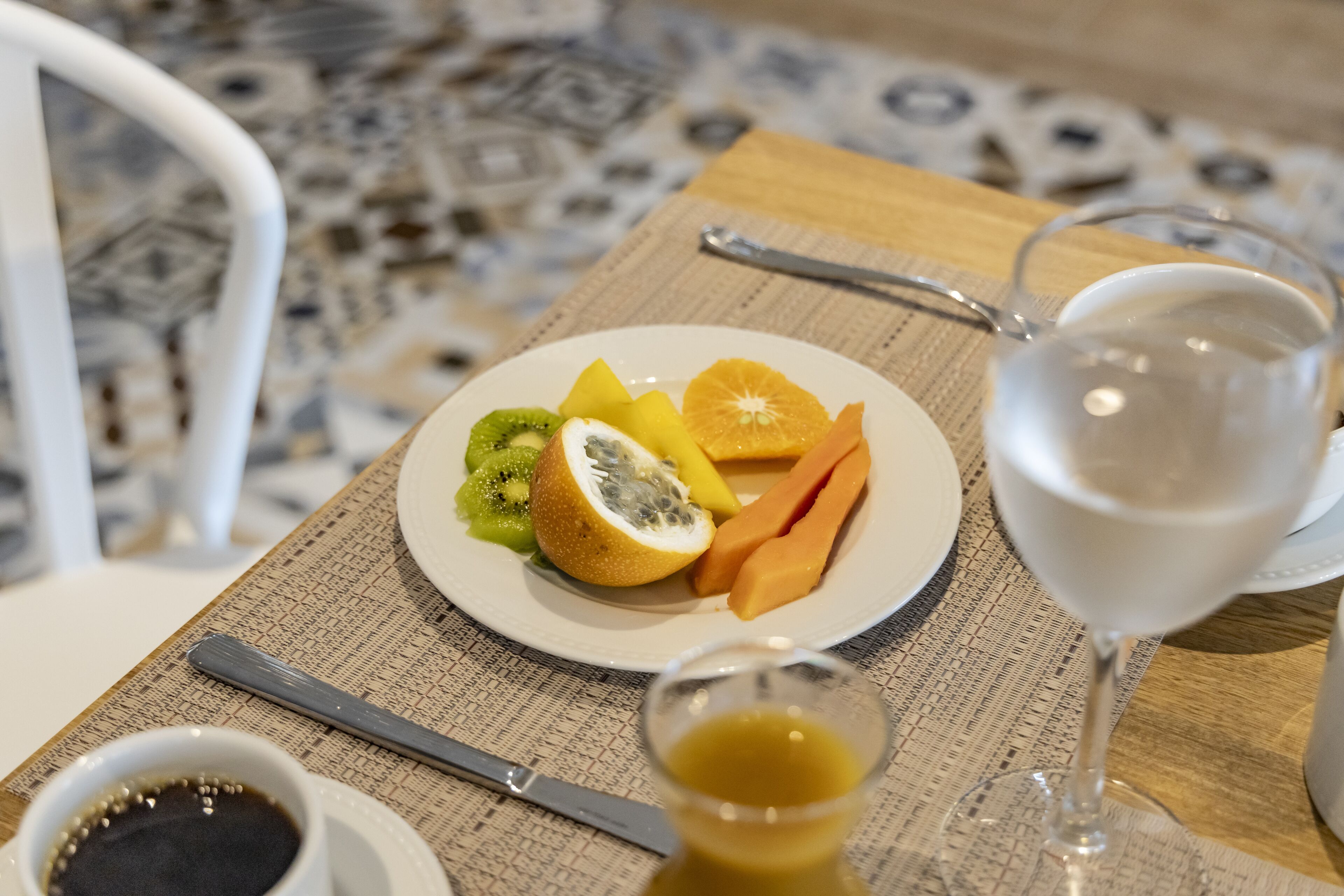 Une table à manger avec une assiette de fruits, un verre d’eau et un petit bol de sauce.