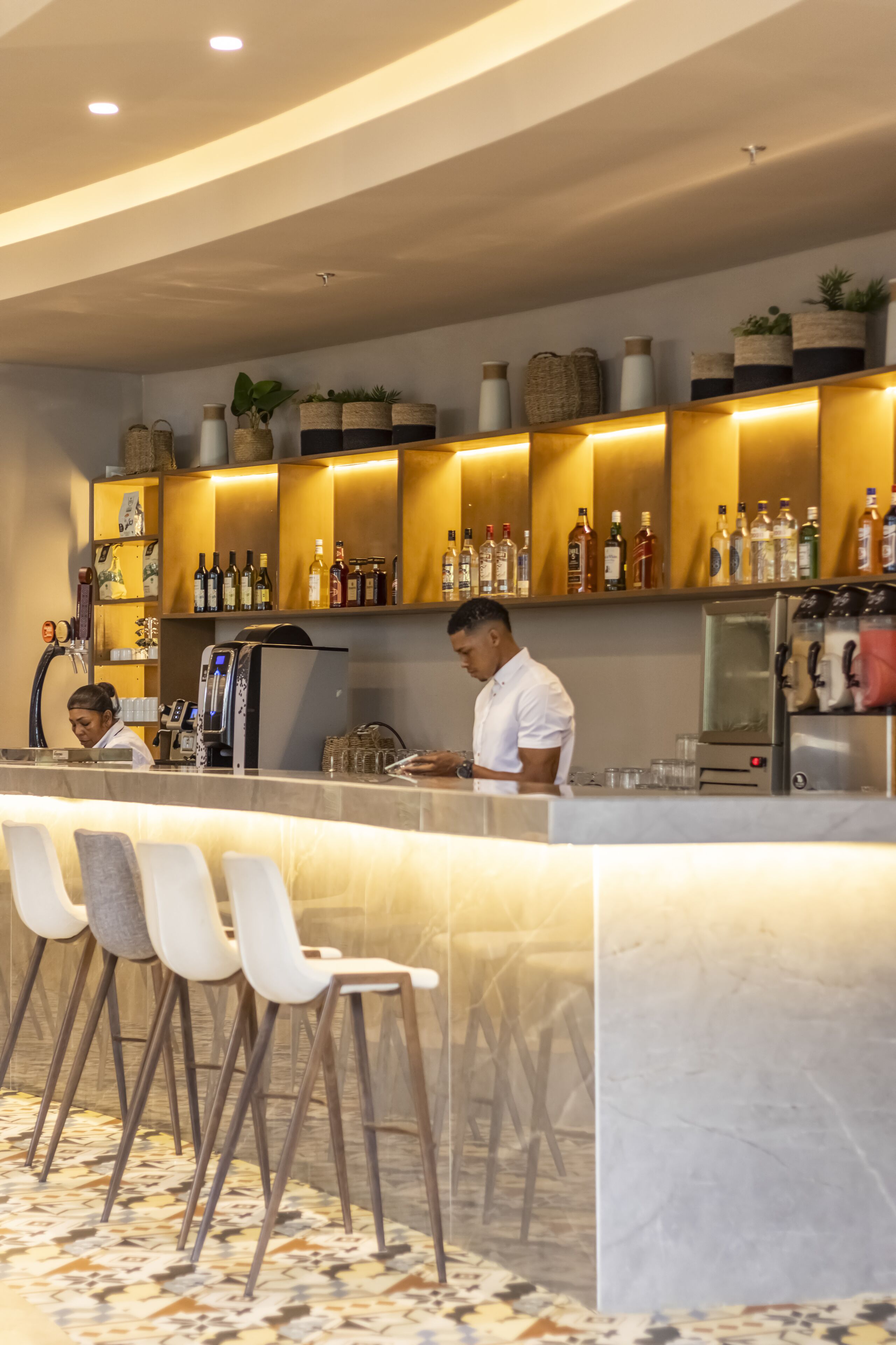 Un espace bar moderne avec un comptoir en marbre, des tabourets de bar blancs et des étagères remplies de bouteilles.