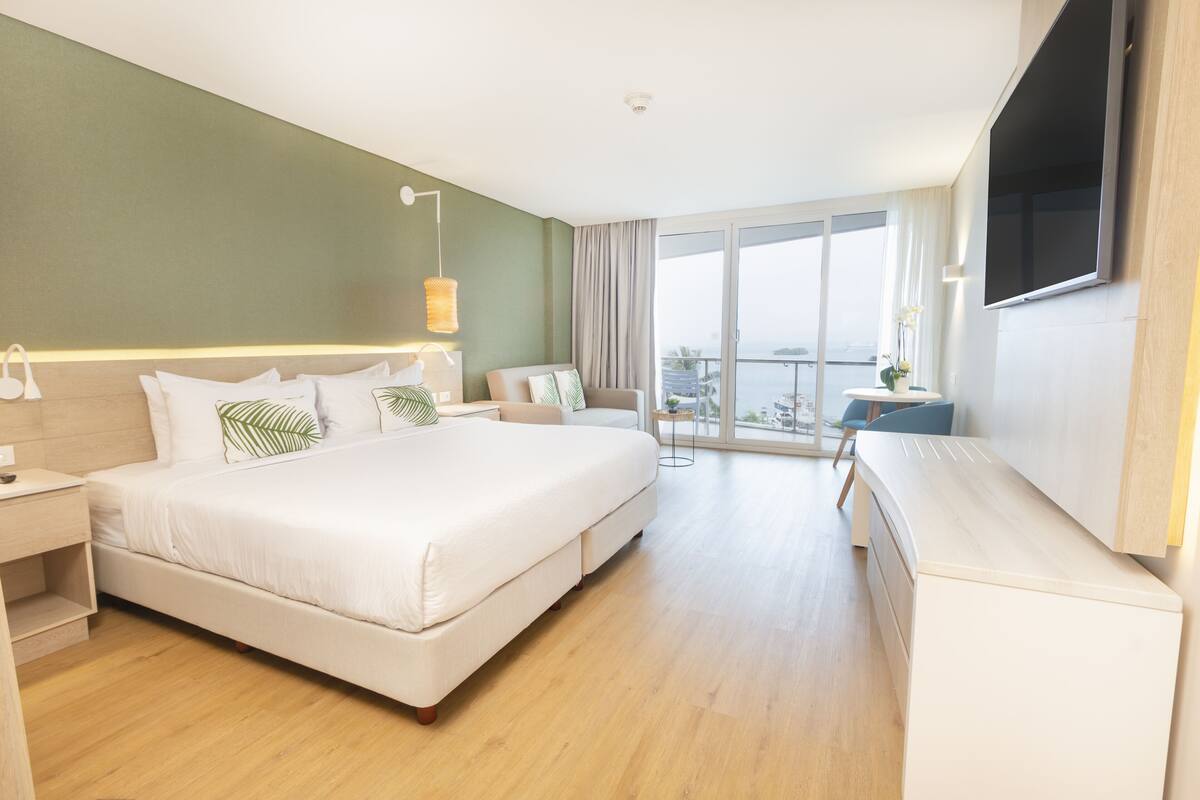 Une chambre d’hôtel moderne avec un grand lit, un bureau et un balcon offrant une vue agréable.