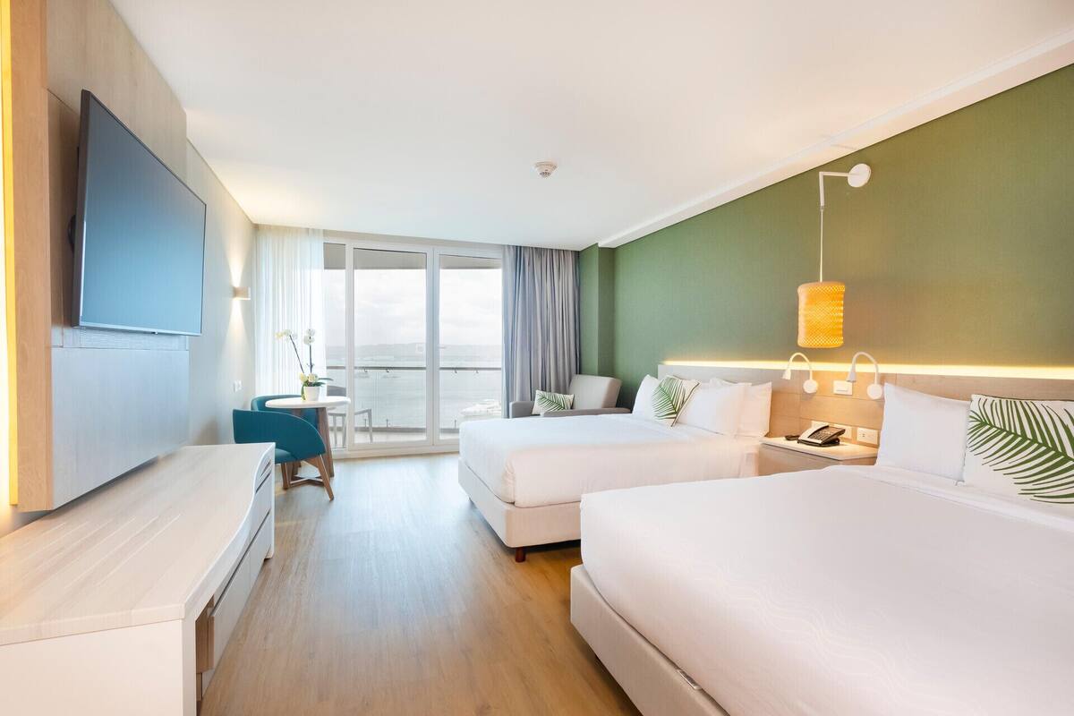 Une chambre d’hôtel avec un balcon, un bureau, deux lits et une télévision.