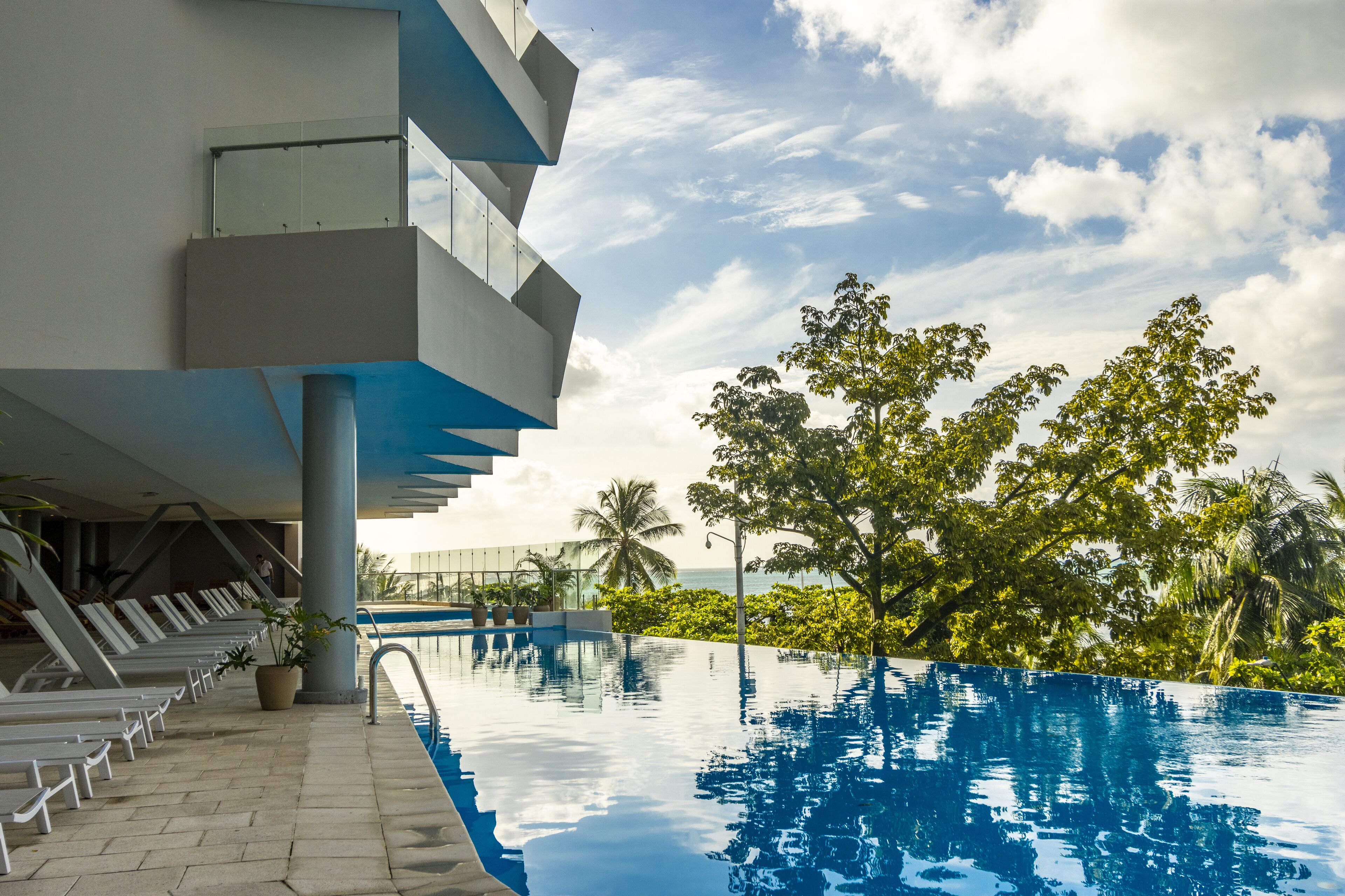 A modern building with a pool area, lounge chairs, and a view of the ocean.