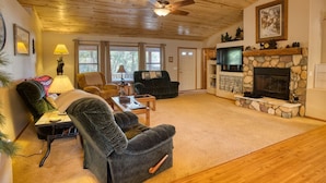 A cozy living room with a stone fireplace, a ceiling fan, and a television.