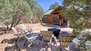A log cabin with a porch, surrounded by trees and outdoor seating.