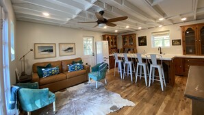 A spacious living area with a brown leather sofa, teal armchairs, and a white fur rug. A dining area with white chairs and a wooden table is adjacent to a kitchen with wooden cabinets and a refrigerator. - Monthly Rental Well Appointed Cottage in the Heart of WA near DT Chs & Beaches. (Charleston)