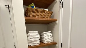 A storage closet with shelves holding folded towels and a wicker basket. - Monthly Rental Well Appointed Cottage in the Heart of WA near DT Chs & Beaches. (Charleston)