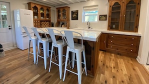 A kitchen with a central island, white chairs, wooden cabinets, and a refrigerator. - Monthly Rental Well Appointed Cottage in the Heart of WA near DT Chs & Beaches. (Charleston)