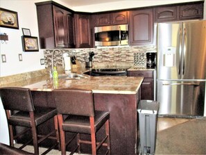 Una cocina con armarios de madera oscura, un refrigerador de acero inoxidable, un microondas y un salpicadero de azulejos.