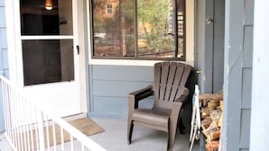 Eine Veranda mit einem Moskitonetz-Schutztür, einem einzelnen Sessel und einem Fenster mit Blick auf Bäume und ein Gebäude.