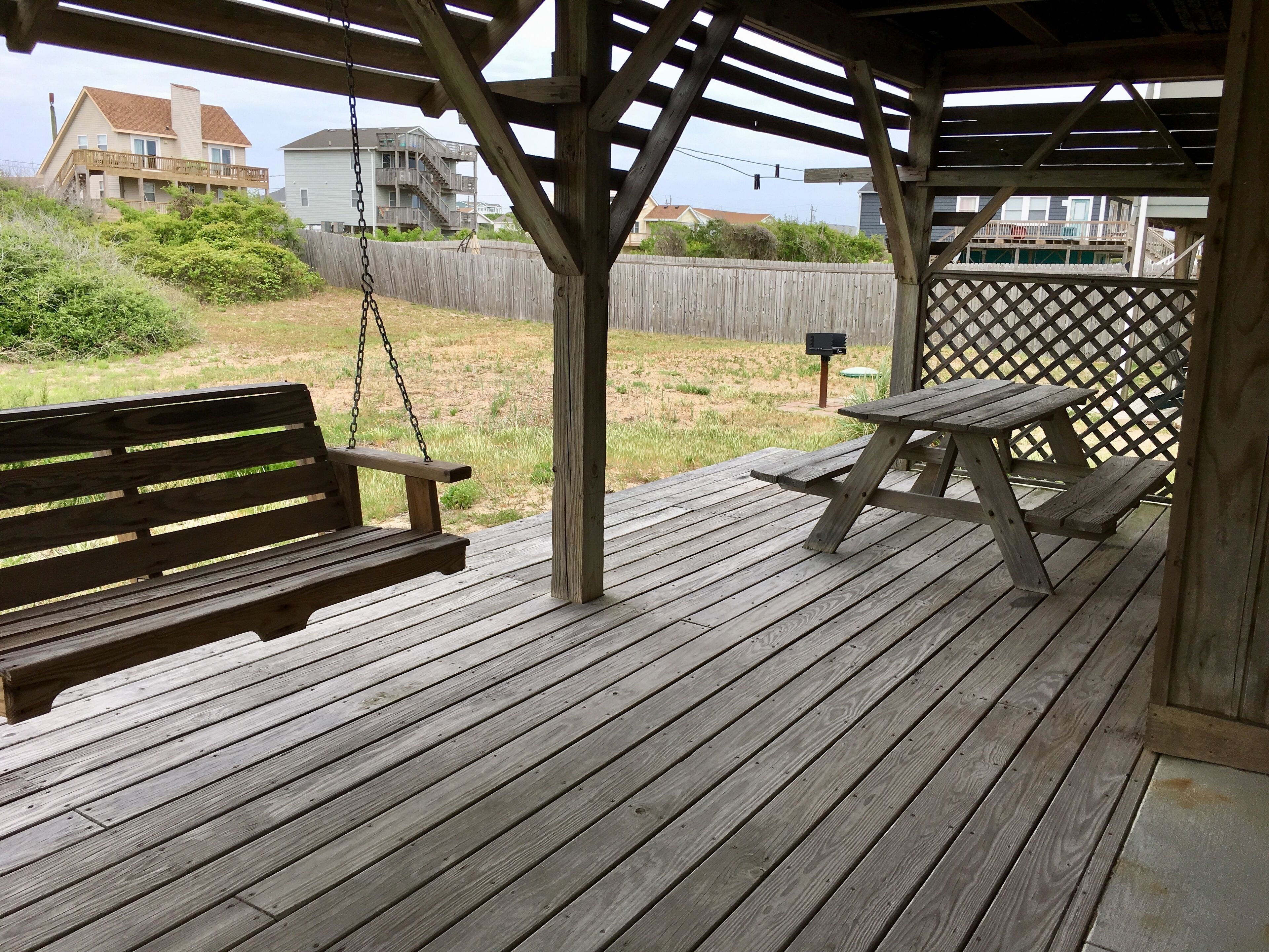 A wooden deck with a bench and picnic table, surrounded by a wooden fence and houses in the background.