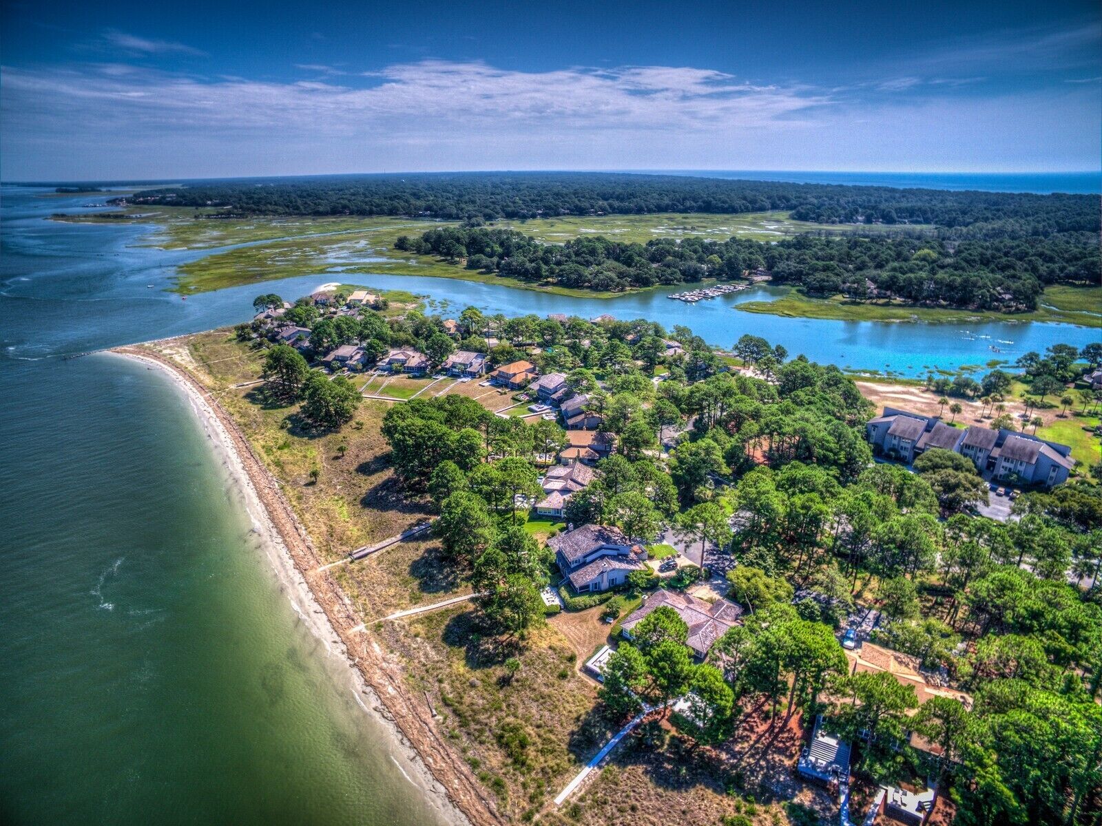 An aerial view of a coastal residential area with houses, a beach, and a lake.