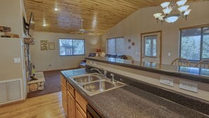 Una cocina con encimeras de granito, lavamanos de acero inoxidable, armarios de madera y un ventilador de techo.