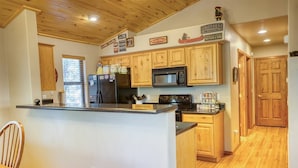 Cocina con armarios de madera, microondas, refrigerador y comedor con una silla.
