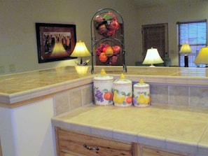 A kitchen with a fruit-themed spice rack, a framed picture on the wall, and two lamps on the countertop.
