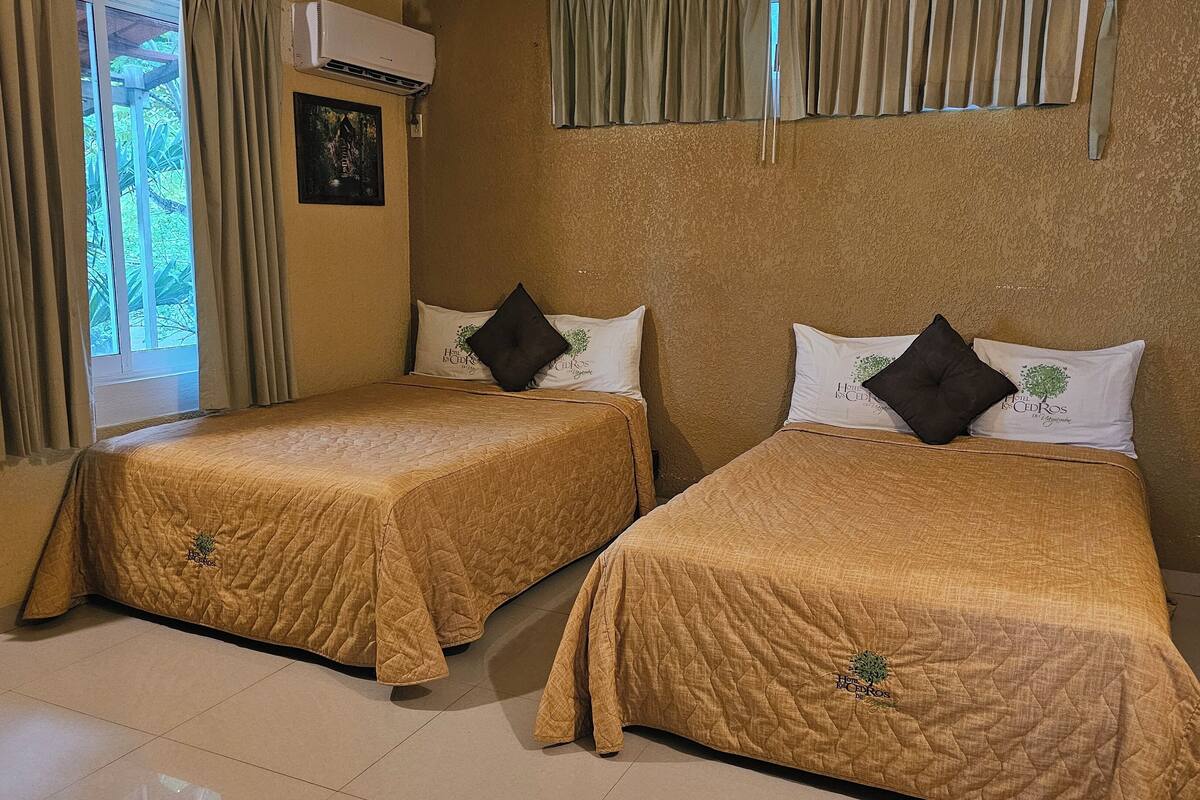 Dos camas individuales con cabeceras y pies de cama a juego, cada una con una almohada y un pequeño logotipo en la colcha.