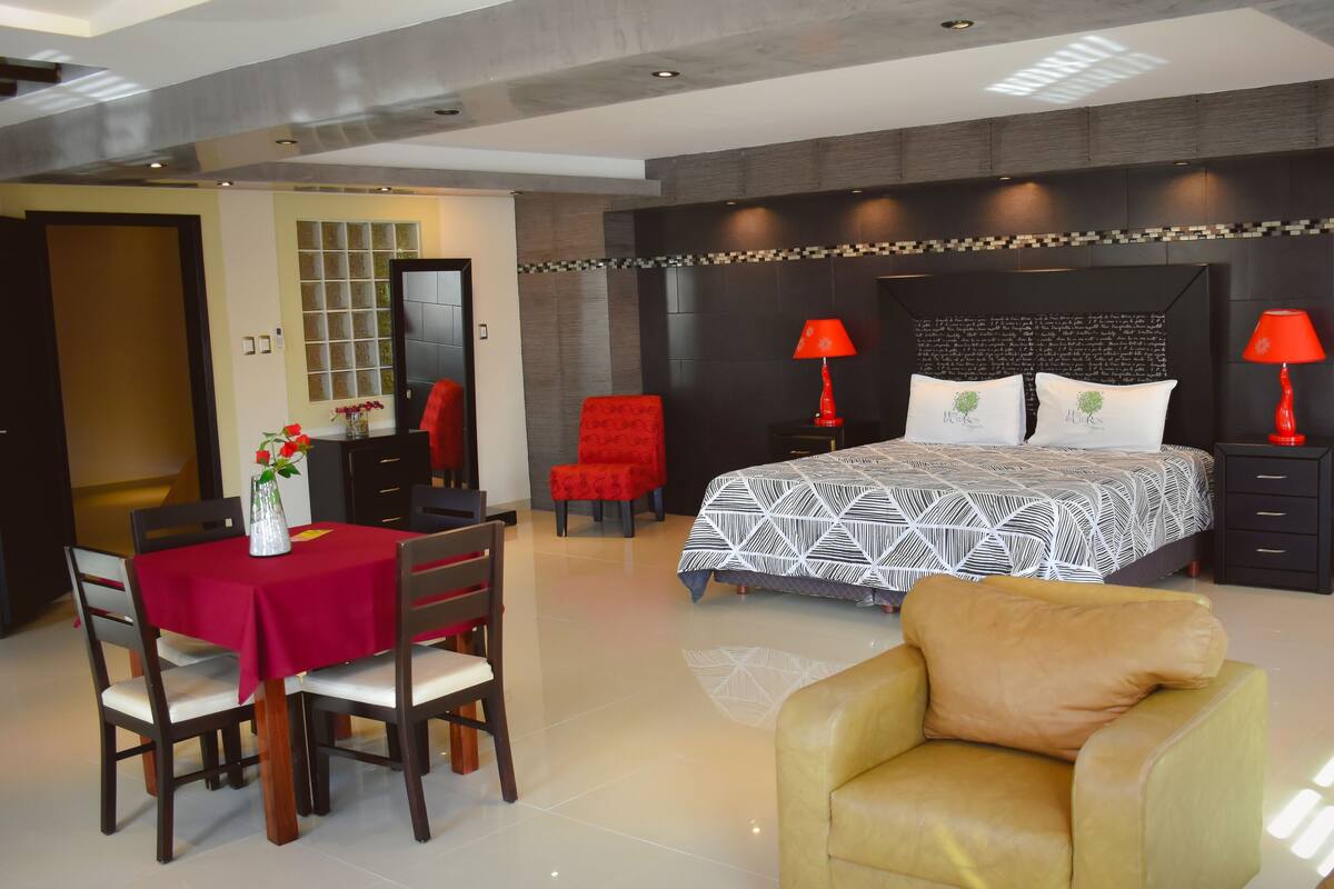 Una habitación de hotel moderna con una cama grande, dos lámparas rojas, una mesa de comedor roja y un sillón amarillo.