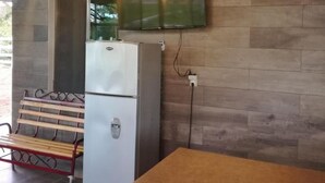 A kitchen area with a wooden wall, a refrigerator, a bench, and a table with two remote controls on it. - Hotel Los Cedros Uayamon (Uayamon)