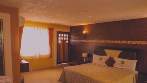 A bedroom with a large bed, a nightstand with a lamp, a window with curtains, and a tiled floor. - Hotel Los Cedros Uayamon (Uayamon)