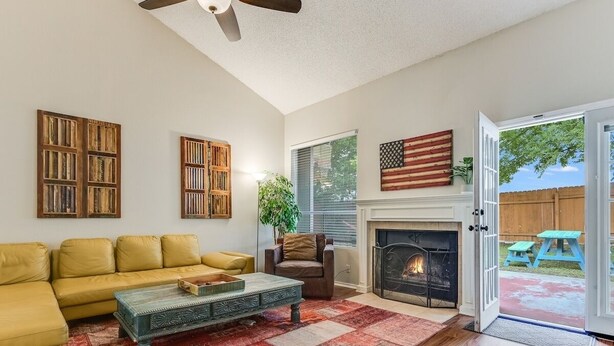 A living room with a yellow sofa, a coffee table, a fireplace, and a view of the backyard through an open door. - Great Home in Austin's Wells Branch Neighborhood! (Austin)