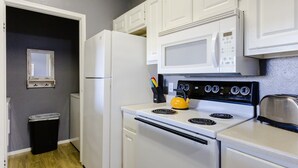 Una cucina compatta con elettrodomestici bianchi, tra cui fornello, forno a microonde e frigorifero.