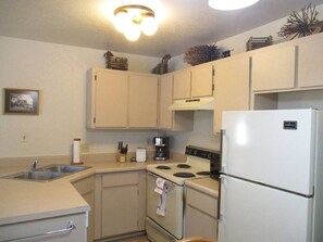 A compact kitchen with a sink, stove, and refrigerator, featuring light-colored cabinets and a small countertop.