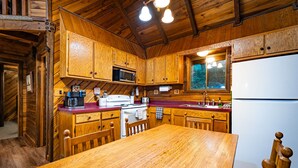 Cocina de cabaña de madera con una mesa de madera, armarios, un refrigerador, un microondas y un fregadero.