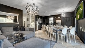 En moderne stue med en grå sofa, et glasbord og et spiseområde med hvide stole og et stort bord.