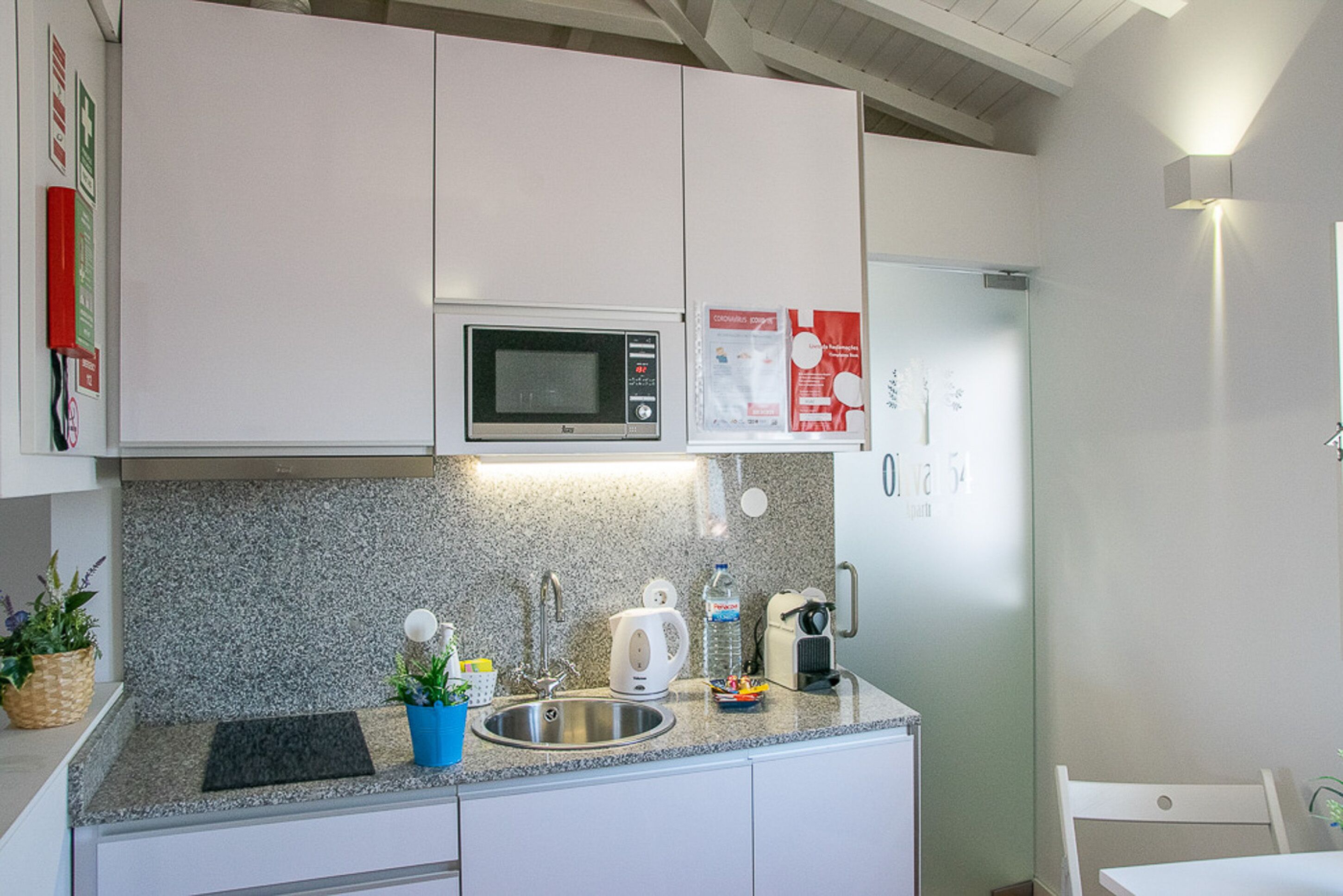 Une cuisine moderne avec des meubles blancs, un plan de travail en granit, un four à micro-ondes, une bouilloire et un réfrigérateur.