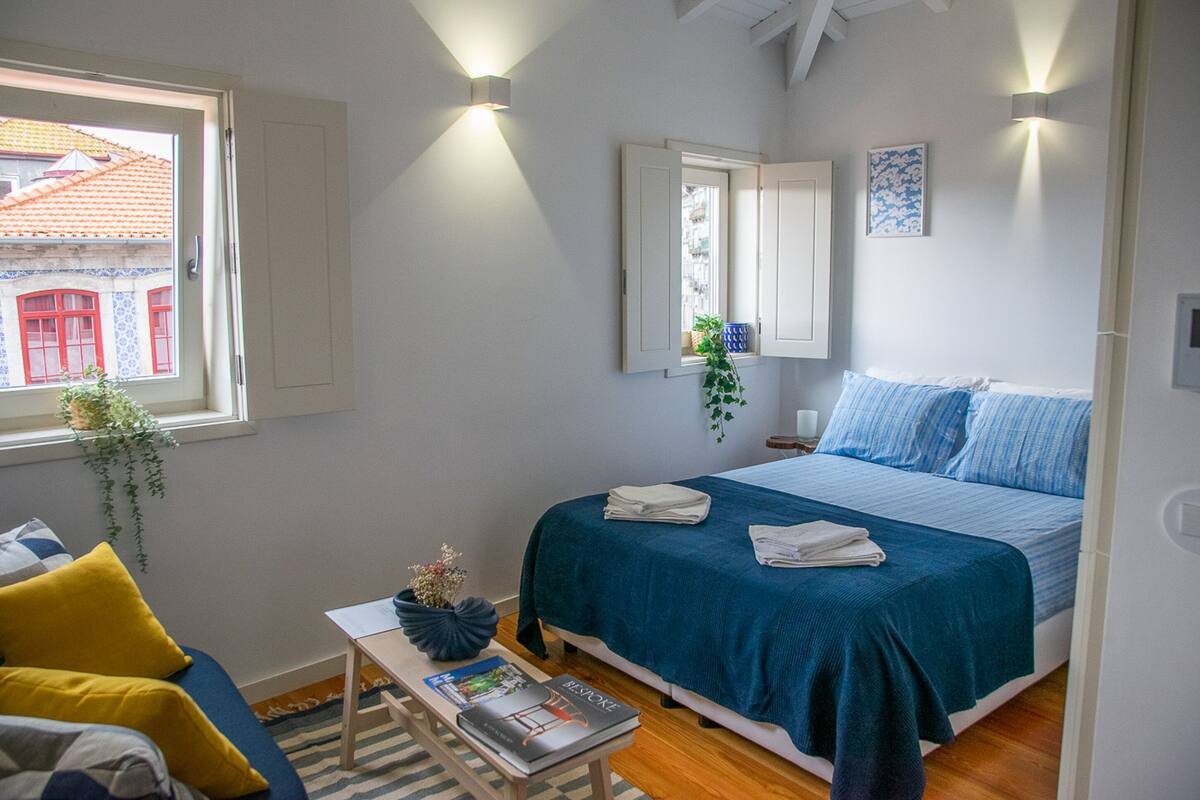A bedroom with a bed, a window, a bedside table, and a chair.