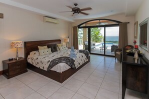 A spacious bedroom with a large bed, a desk, and a view of the ocean through a sliding glass door. - Casa Antonelli (Sardinal)