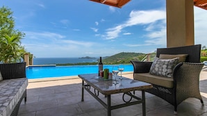 An outdoor patio with a pool, wicker furniture, and a view of the ocean. - Casa Antonelli (Sardinal)