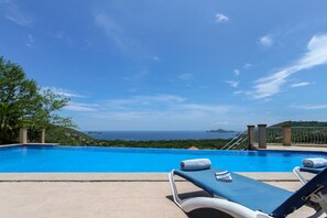 A pool with two lounge chairs and a towel, overlooking a scenic view of the sea and hills. - Casa Antonelli (Sardinal)