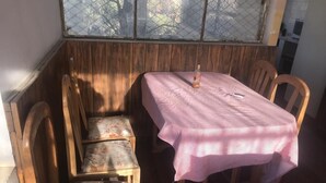Una mesa de comedor de madera con mantel a cuadros rosa y una botella de licor. Hay cuatro sillas de madera con tapicería floral.