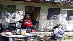 Un entorno rústico al aire libre con una mesa redonda, una silla y una persona de pie.