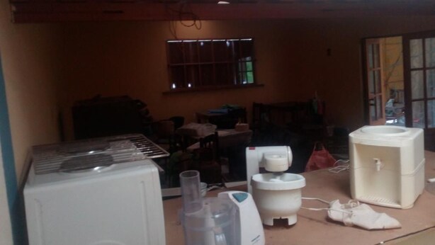 Habitación compacta con área de kitchenette que incluye un refrigerador, licuadora, cafetera y lavamanos. Hay una ventana con rejas y una puerta que da a otra habitación.